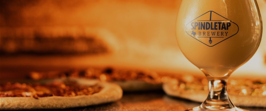 pint of beer and pizza sitting in front of fire pizza oven